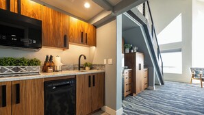 A modern kitchen with wooden cabinets, a built-in microwave, and a dishwasher. There's a staircase leading to a loft area with a view of the outdoors. - Seaside Oceanfront Inn (Seaside)