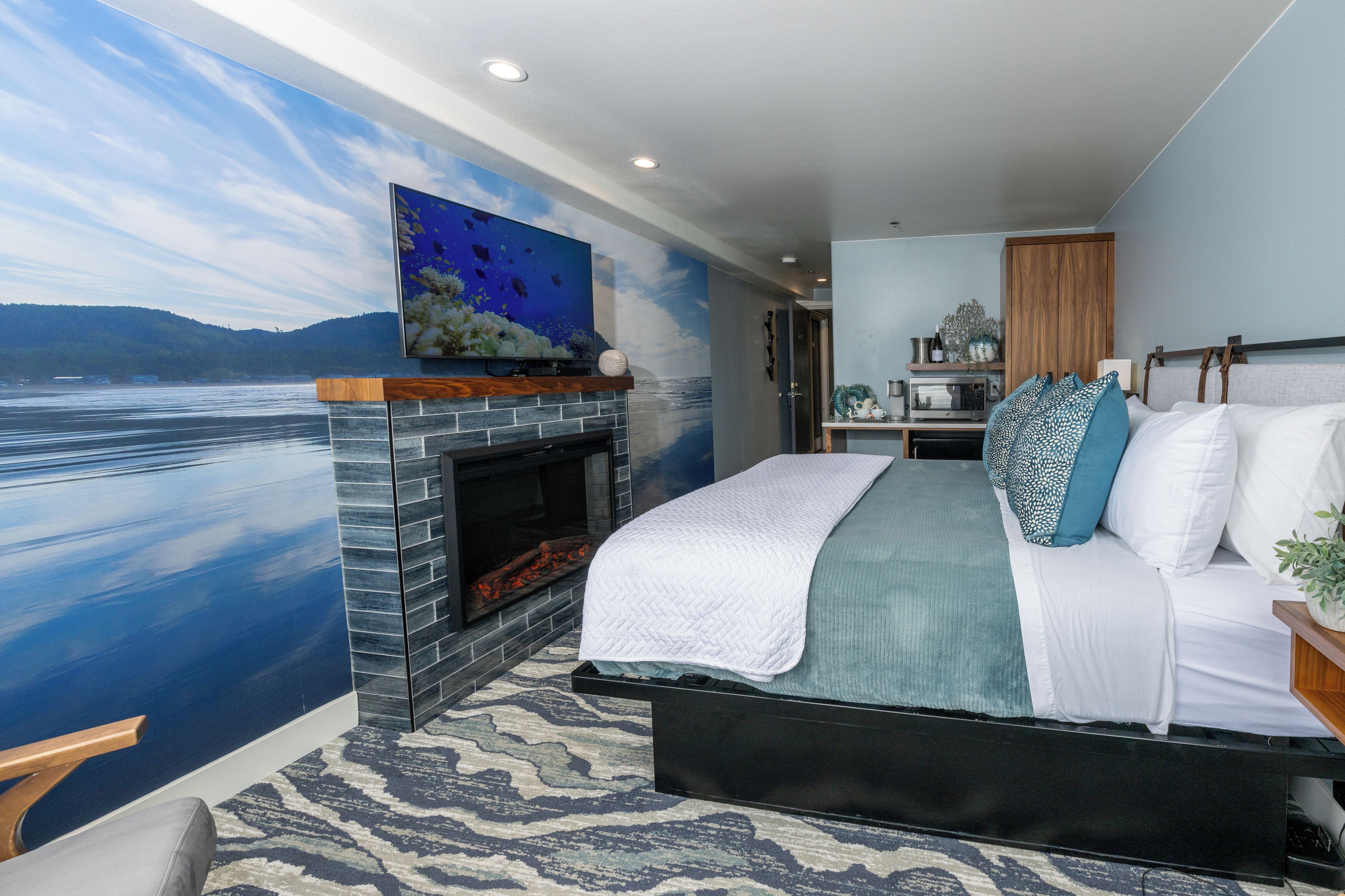 A bedroom with a large bed, a fireplace, and a mural of a lake.