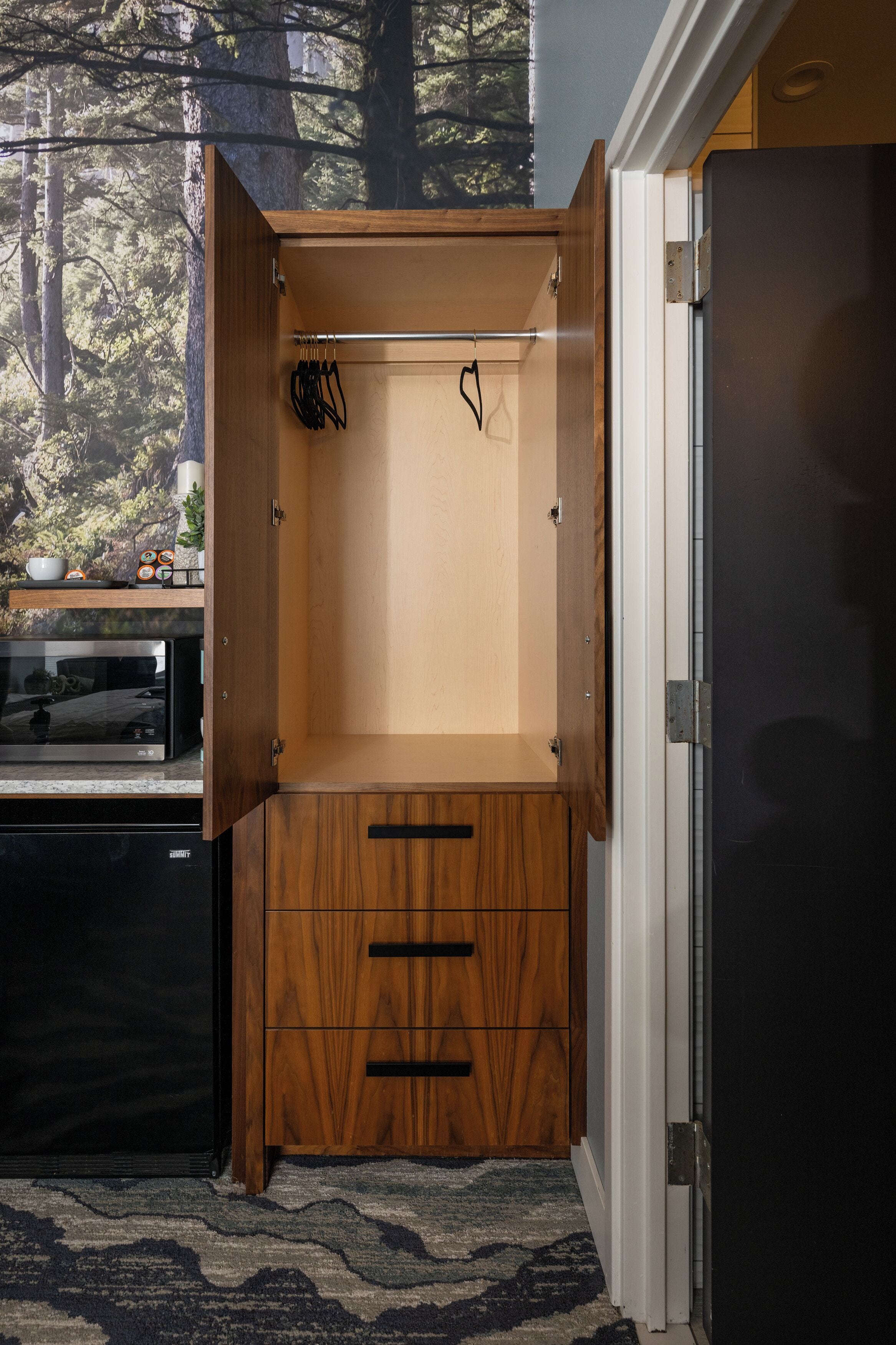 A compact kitchen with a built-in microwave, wooden cabinets, and a view of trees through a window.