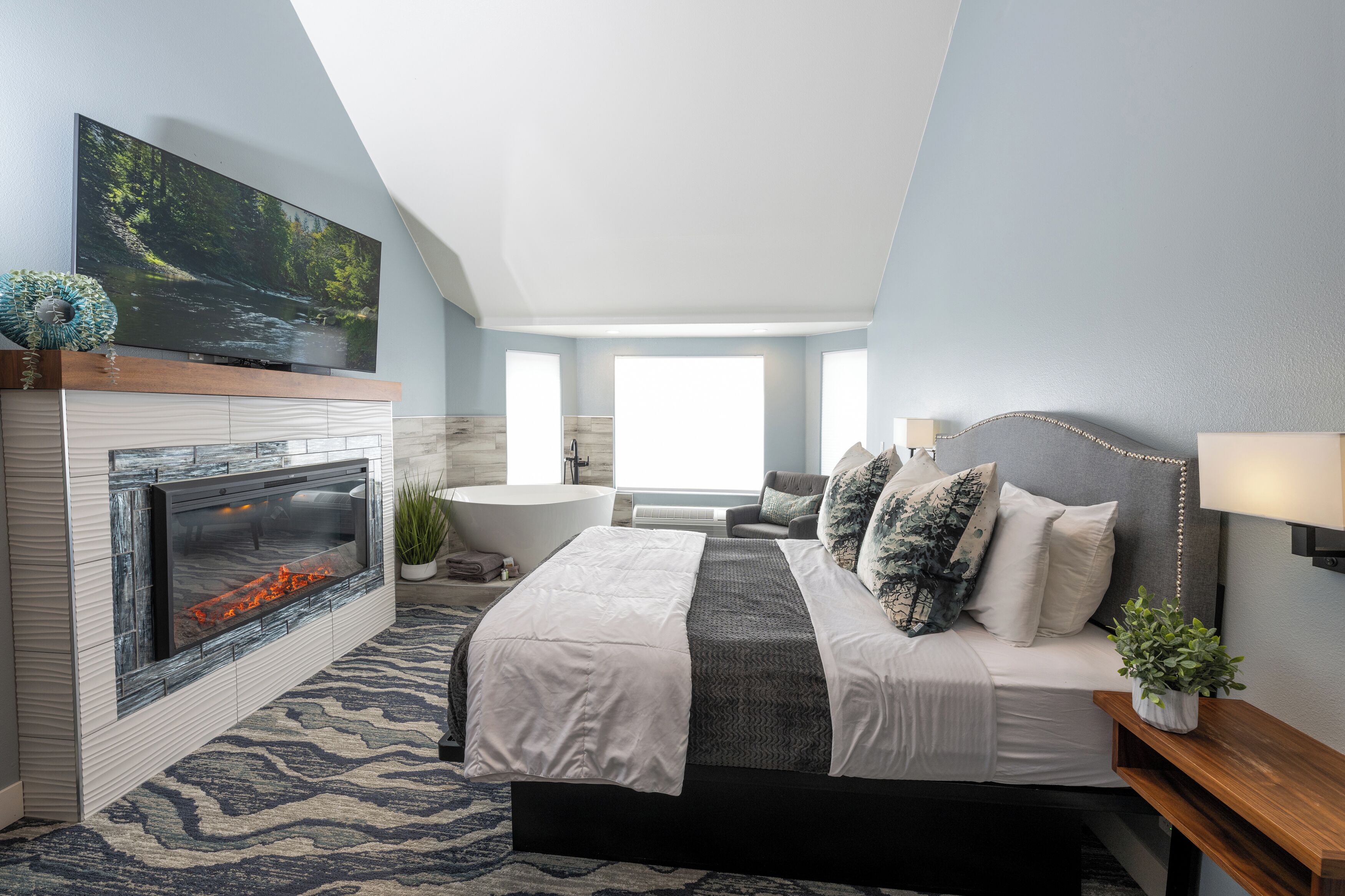 A modern bedroom with a fireplace, a large bed, a sofa, and a TV mounted on the wall.