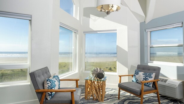 A spacious room with large windows offering ocean views, a chandelier, and two upholstered chairs with decorative pillows. - Seaside Oceanfront Inn (Seaside)