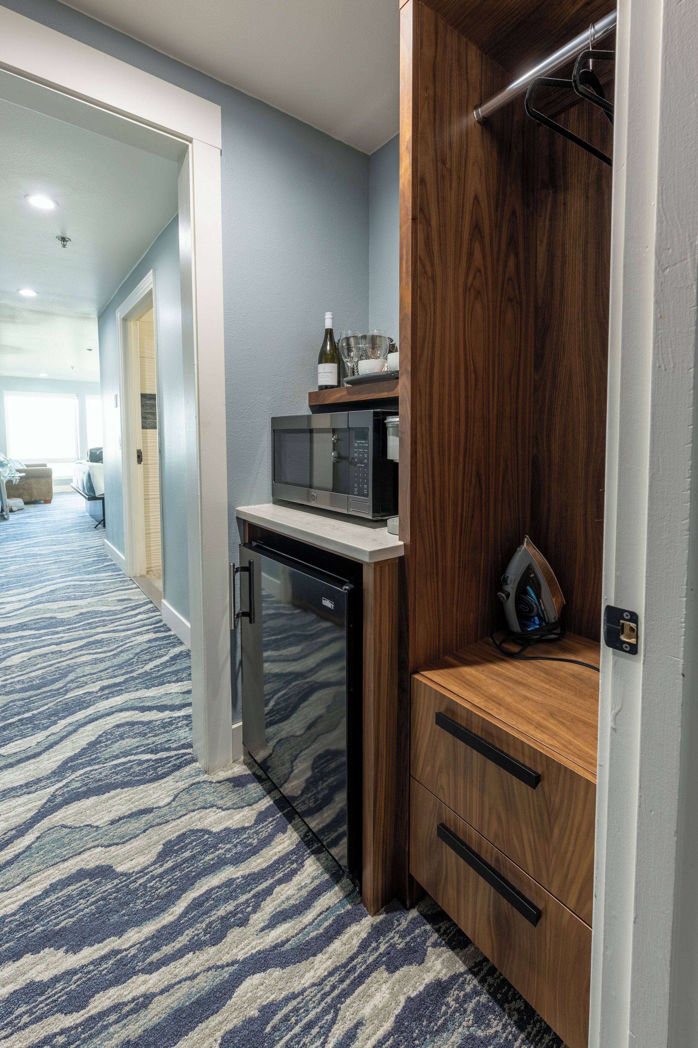 A compact kitchen with a microwave, a dishwasher, and a wine bottle on a shelf.