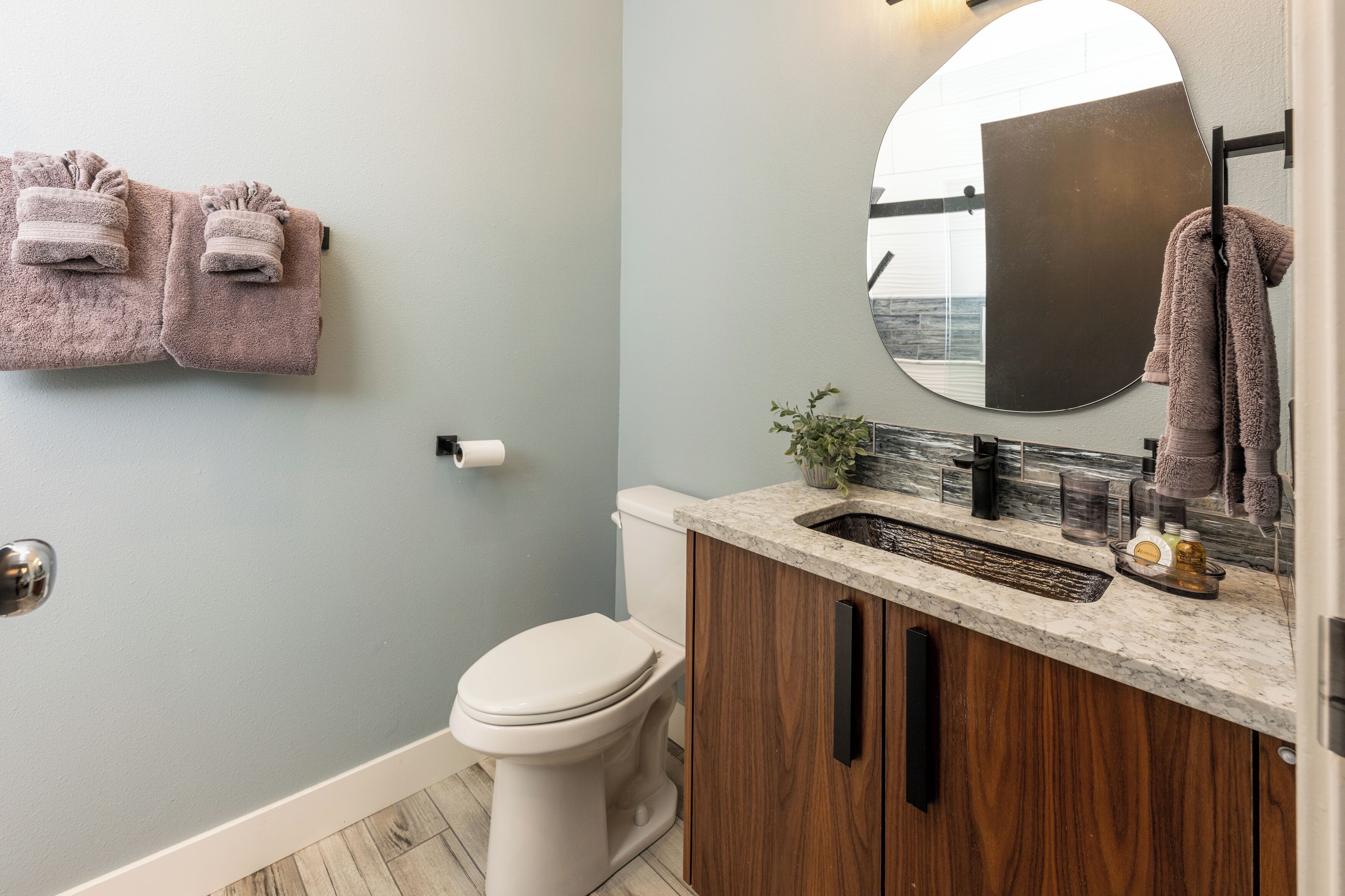 A bathroom with a toilet, a sink with a mirror, and two towels hanging on the wall.