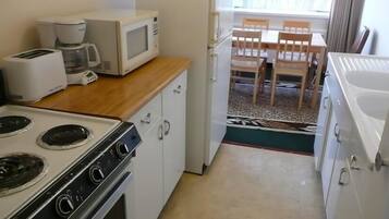 A compact kitchen with a stove, microwave, and coffee maker. There is a dining area with a table and chairs visible through an open door.