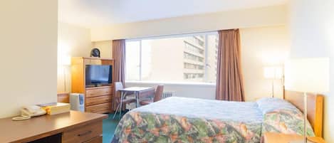 A hotel room with a bed, a desk, a chair, a television, and a window with curtains.