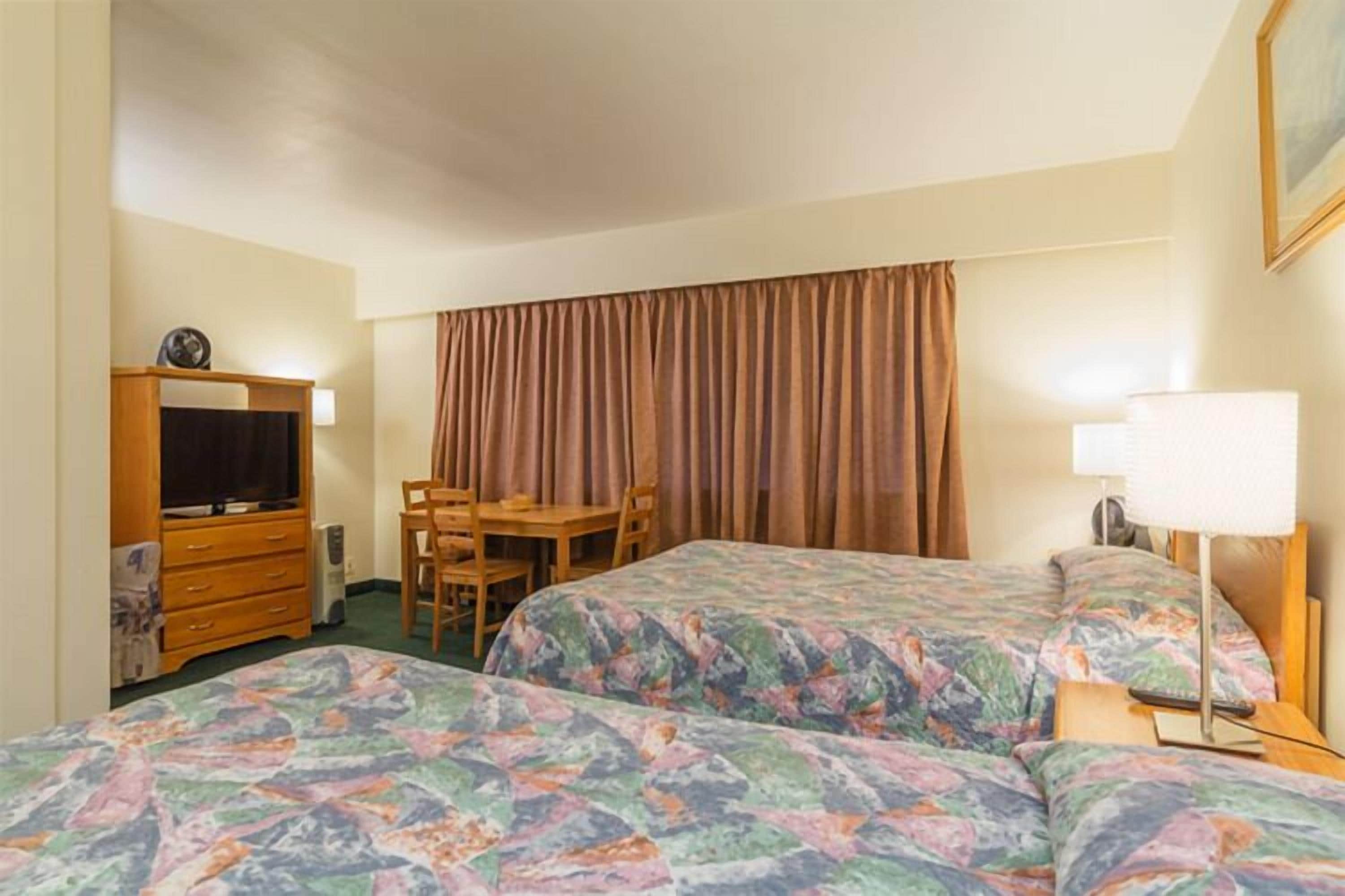 Habitación de hotel con dos camas, un escritorio, una silla, un televisor y una lámpara.