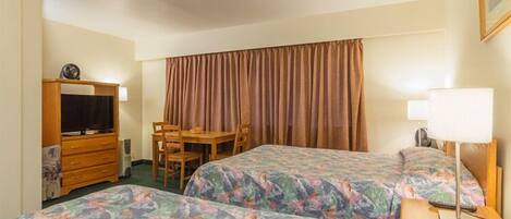 Habitación de hotel con dos camas, un escritorio, una silla, un televisor y una lámpara.