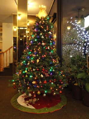 Árvore de Natal com luzes coloridas e enfeites, sobre um tapete vermelho e verde, com uma decoração de Papai Noel na base.