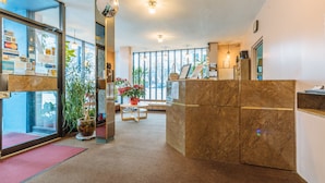 A reception area with a marble counter, a potted plant, and a view of the outdoors through large windows. - English Bay Hotel (Vancouver)