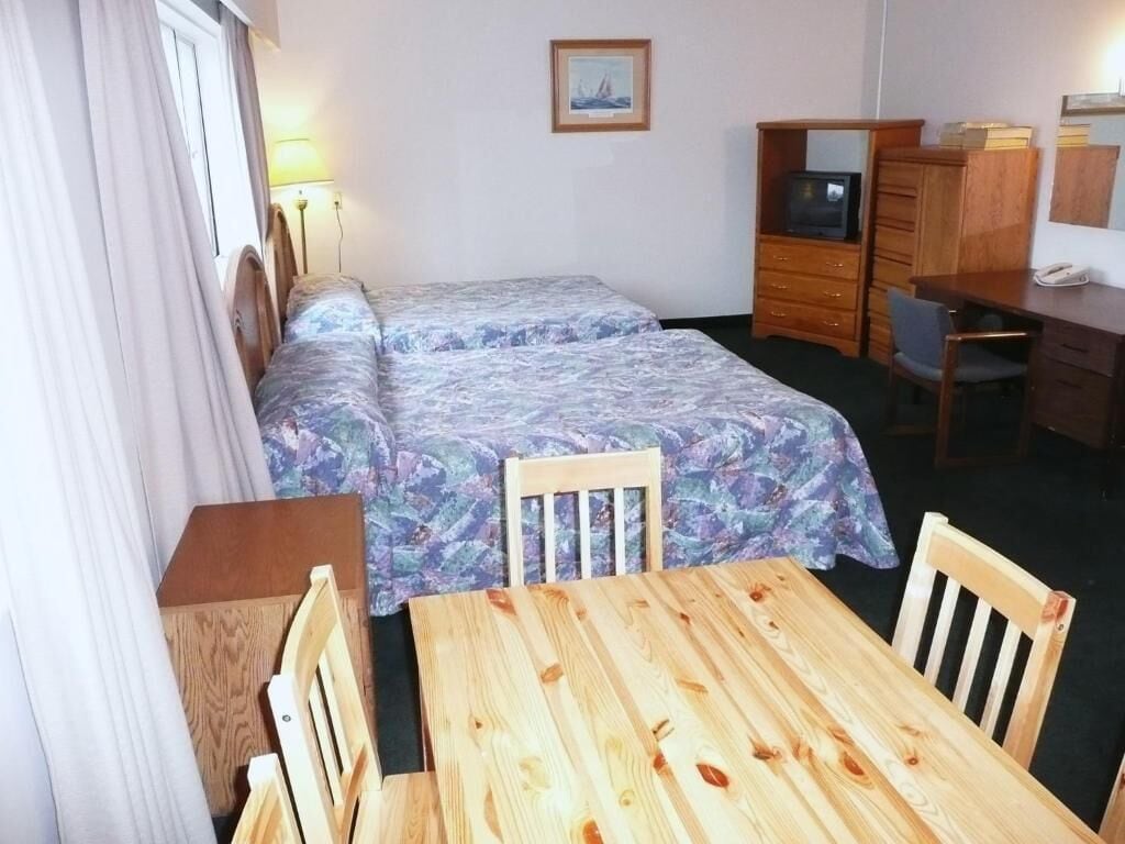 A hotel room with two beds, a wooden table, a desk, and a chair.