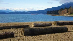 A beach with logs in the foreground and a ship in the distance. - English Bay Hotel (Vancouver)