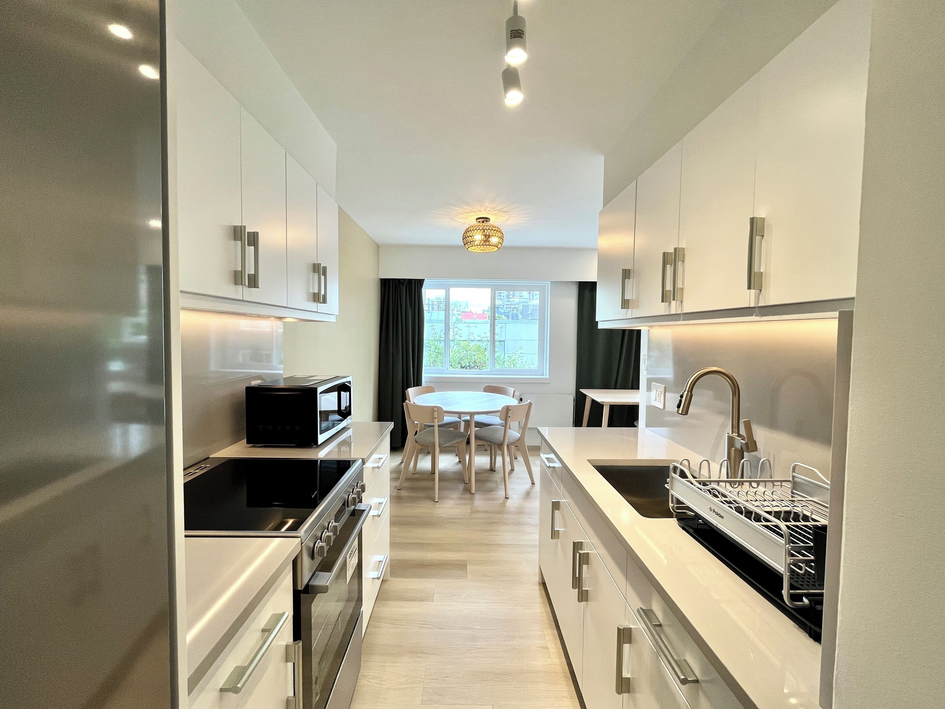 A modern kitchen with stainless steel appliances, a dining area with a round table and chairs, and a window with curtains.