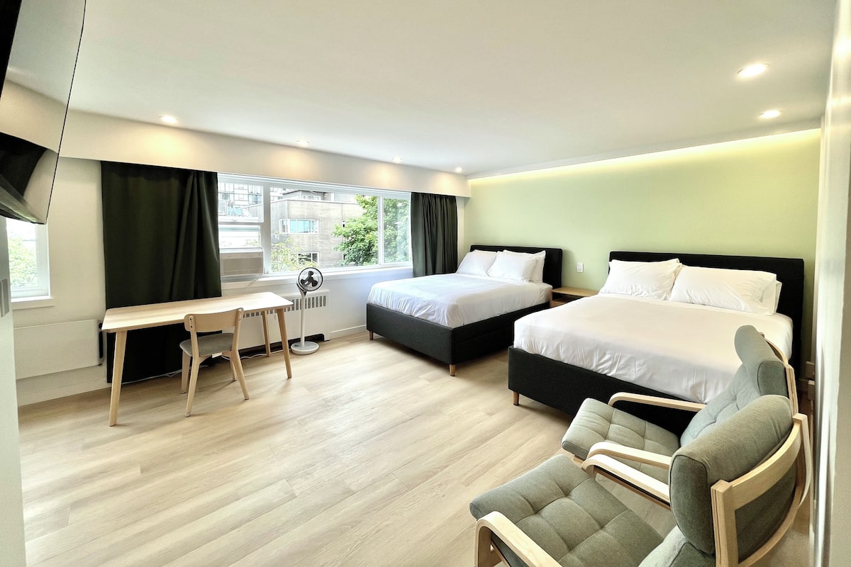 A modern hotel room with two beds, a desk, a chair, and a large window.
