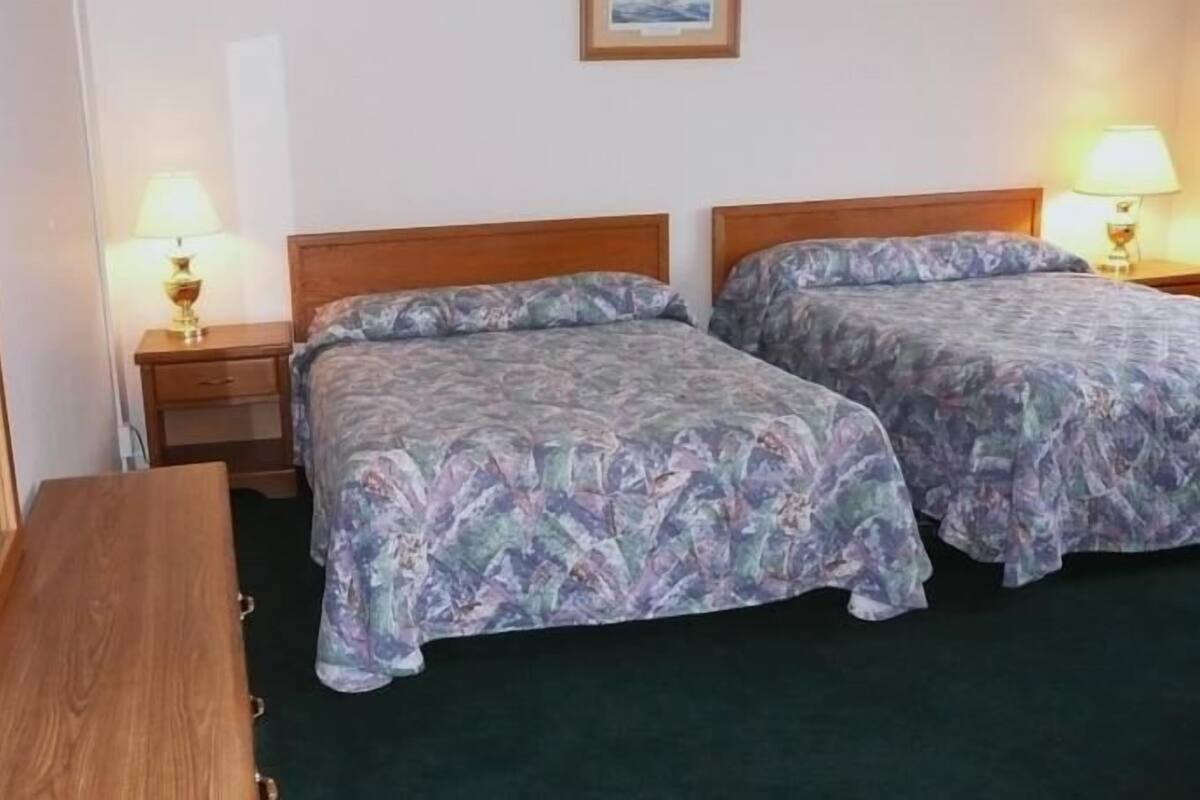 A hotel room with two beds, a wooden bench, a nightstand with a lamp, and a mirror.