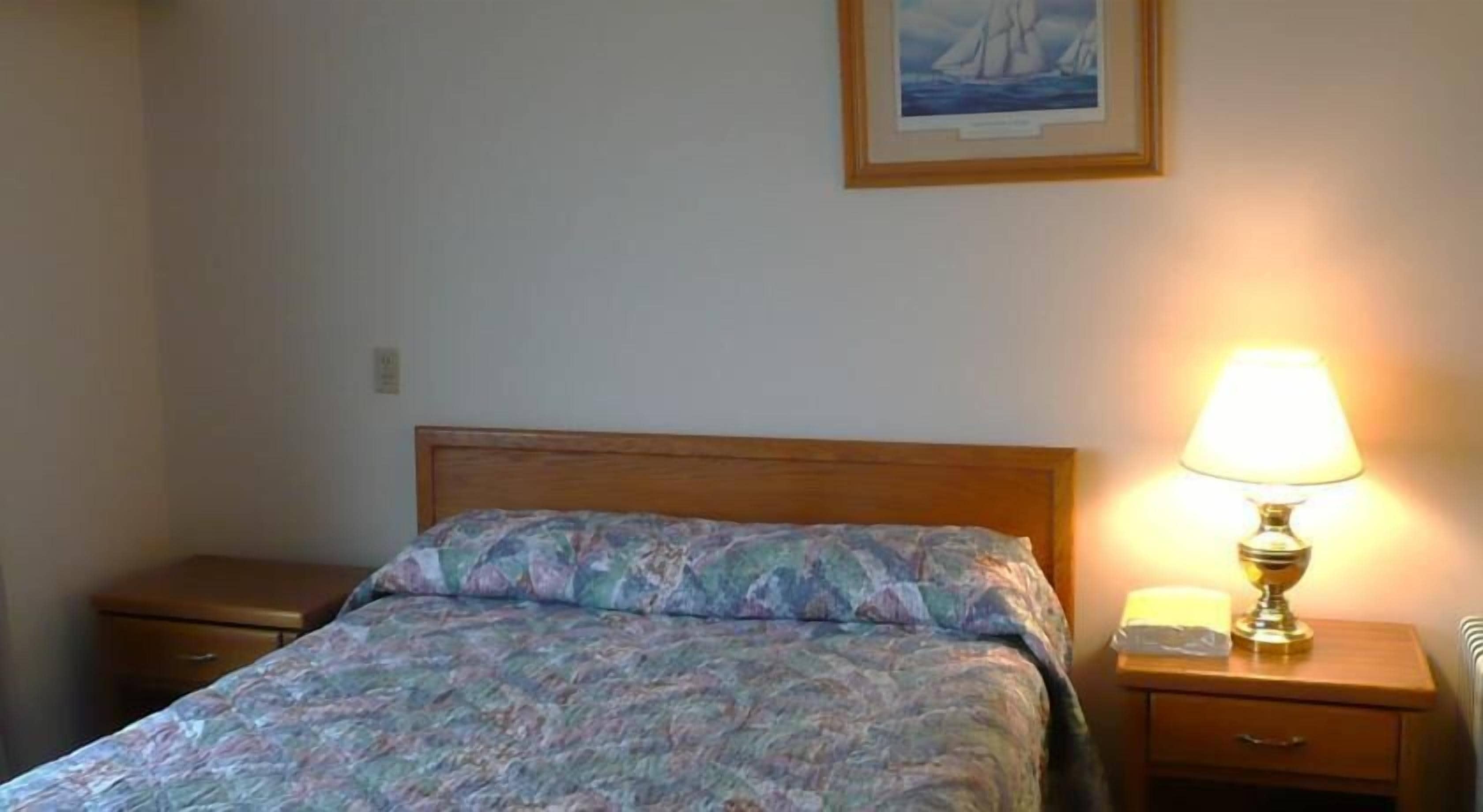 A bedroom with a wooden bed, a nightstand with a lamp, and a framed picture on the wall.