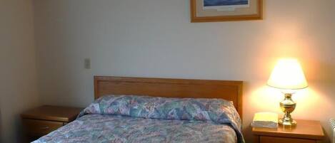 A bedroom with a wooden bed, a nightstand with a lamp, and a framed picture on the wall.