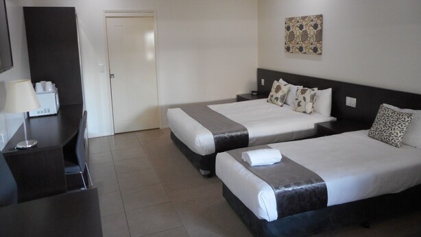 A hotel room with two beds, a desk, a chair, a lamp, and a wall-mounted artwork.