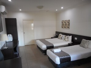 A hotel room with two beds, a desk, a chair, a lamp, and a wall-mounted artwork. - Injune Motor Inn (Injune)