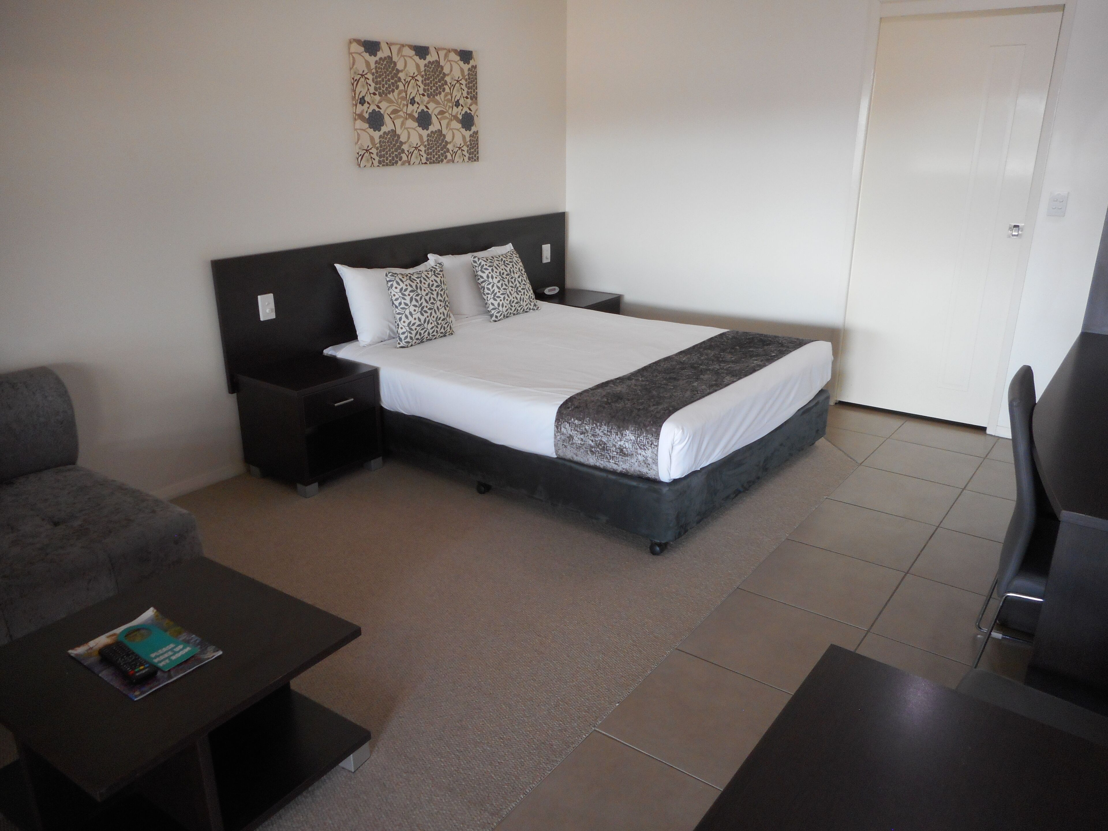 Une chambre d’hôtel bien rangée, avec un lit, des tables de chevet, une chaise et une petite table sur laquelle se trouve un magazine.