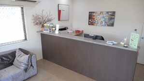 A reception area with a grey reception desk, a sofa, a window with blinds, and two wall-mounted artworks.
