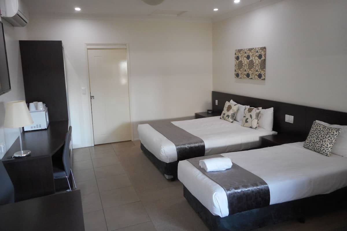 Habitación de hotel con dos camas, un escritorio, una silla, una lámpara, cafetera y una puerta.