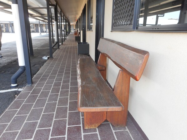 A covered walkway with a wooden bench, brick flooring, and metal railings. - Injune Motor Inn (Injune)