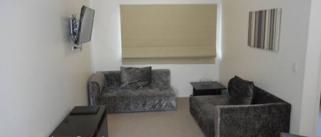 Una sala de estar con dos sofás, un televisor, una mesita y una ventana con persianas.