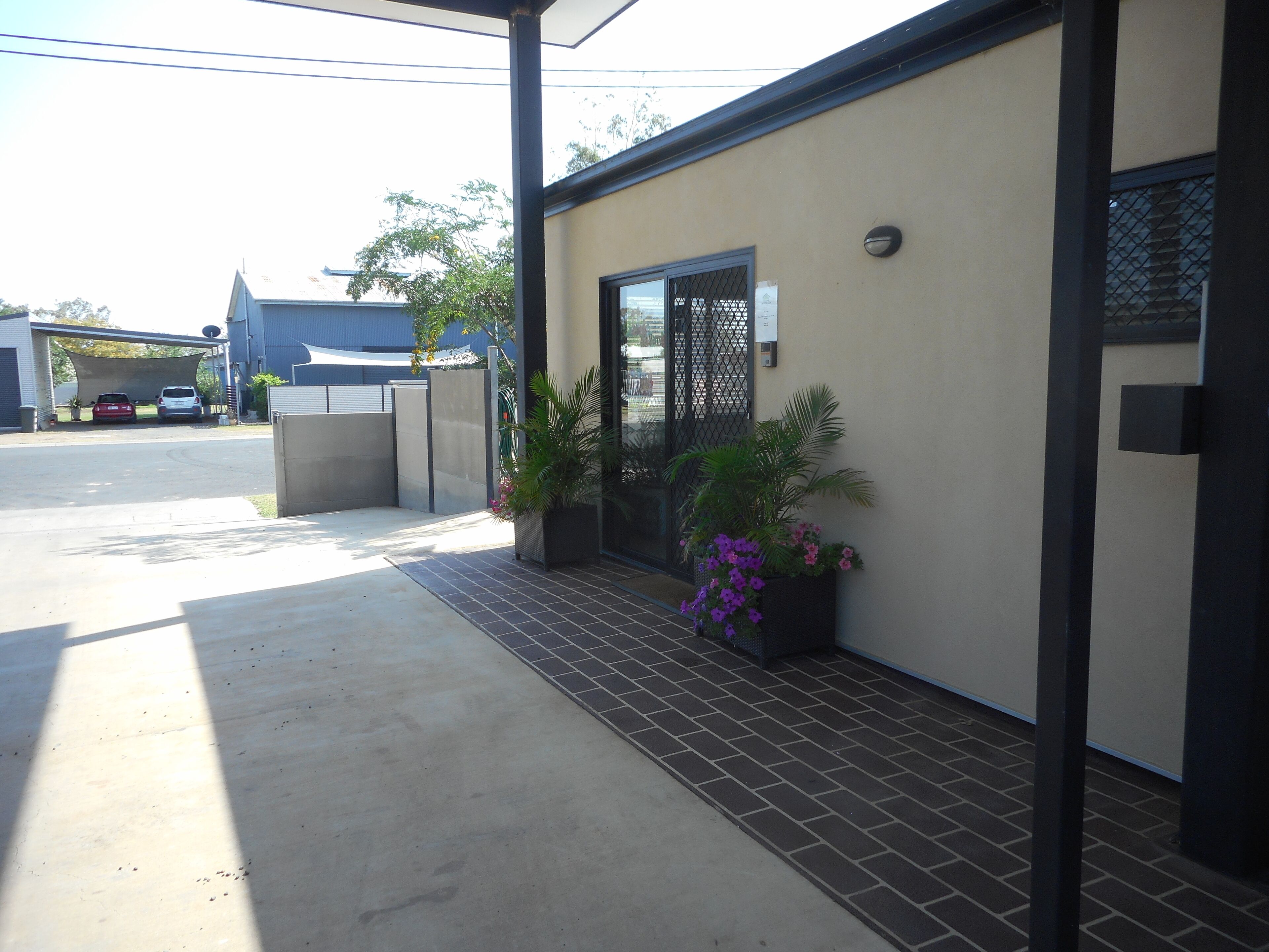 A modern building with a covered driveway, a gated entrance, and potted plants.