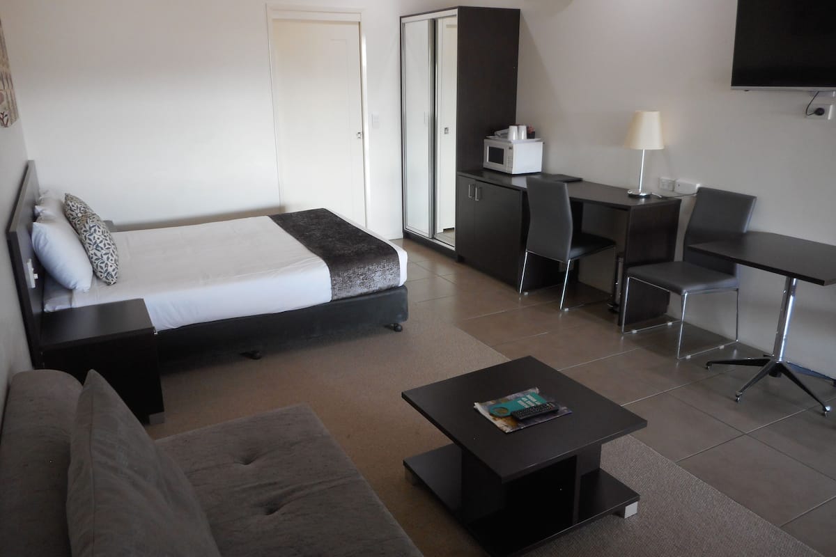 Una habitación de hotel con cama, sofá, escritorio con silla, mesa de centro y televisor.