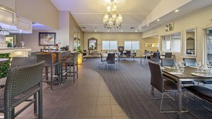 Un vaste espace de restauration dans l’hôtel, avec de nombreuses tables et chaises, un lustre et un coin bar doté de fauteuils en osier.
