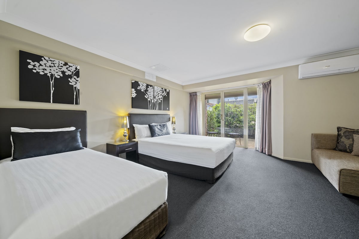 A hotel room with two beds, a sofa, and a large window with curtains.