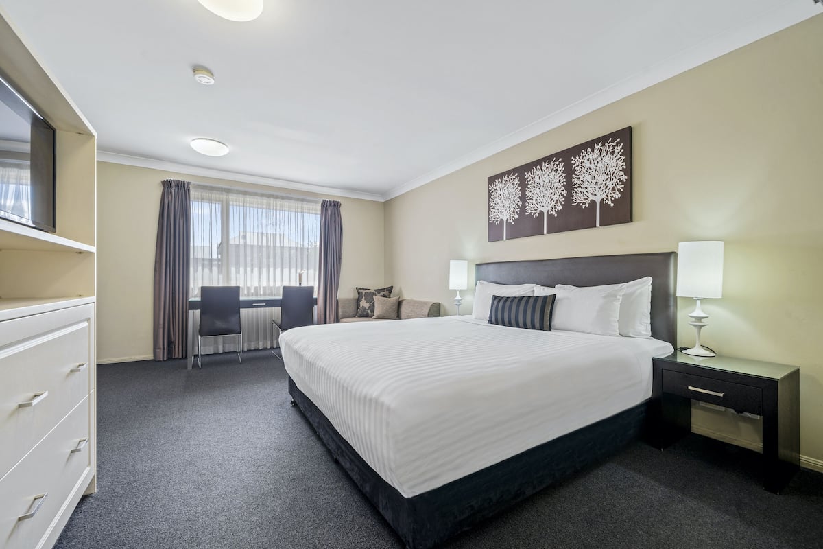 A hotel room with a large bed, a desk, a chair, a nightstand, and a TV.
