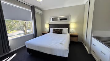 A hotel room with a large bed, two bedside tables with lamps, a ceiling fan, a window with curtains, and a view of the outdoors.