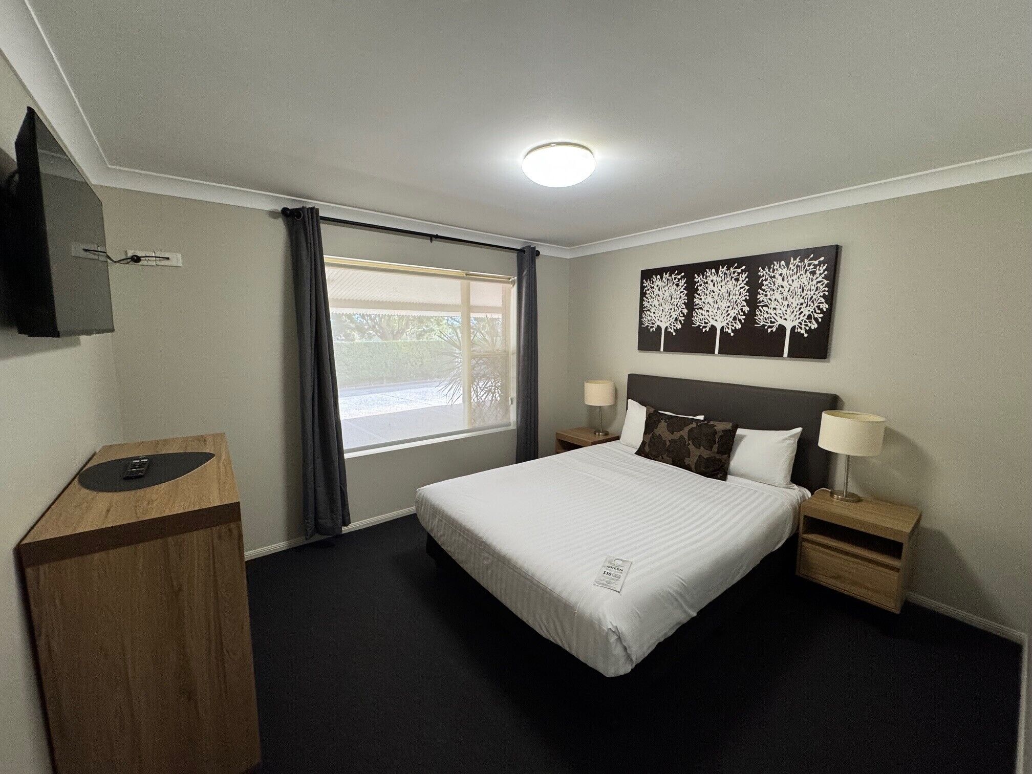 A hotel room with a bed, a desk, a TV, and a window with curtains.