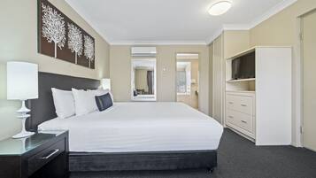 Une chambre d’hôtel avec un grand lit, une table de chevet avec une lampe, une armoire et un téléviseur posé sur un meuble.