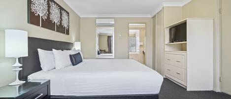 Habitación de hotel con una cama grande, una mesita de noche con lámpara, un armario y un televisor sobre un mueble.