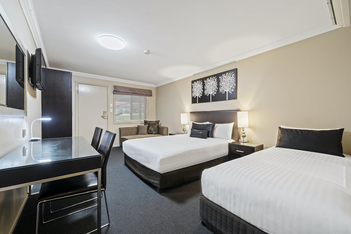 A hotel room with a glass table, two beds, a TV, and a painting on the wall.