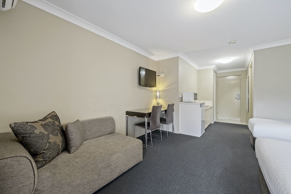 Habitación de hotel con sofá, escritorio con silla, cama y televisión montada en la pared.