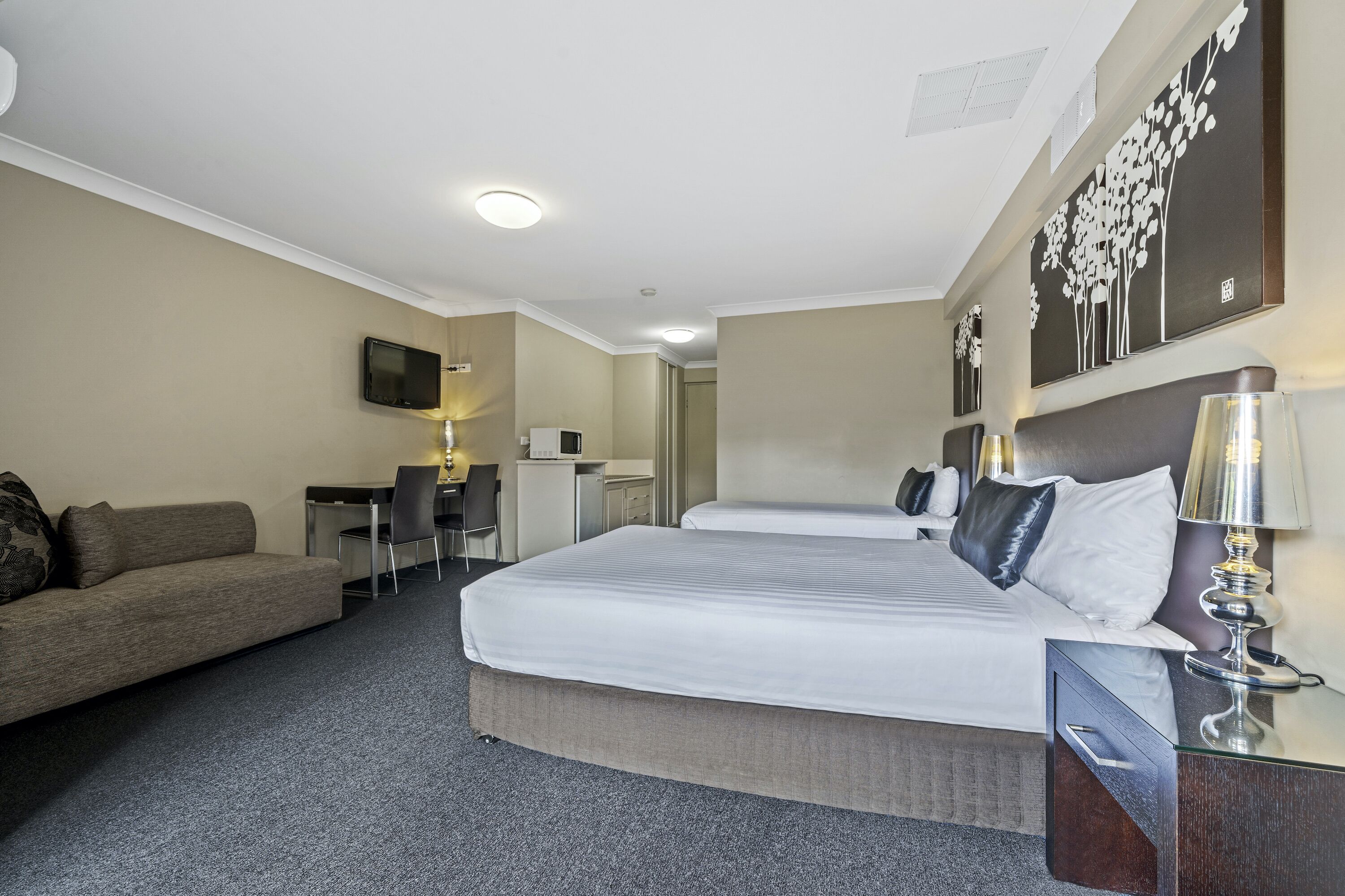A hotel room with a large bed, a desk, a couch, and a TV on the wall.