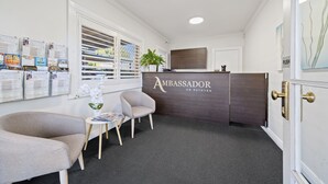 Un espace d’accueil avec un comptoir de réception en bois foncé, une plante en pot et un coin salon composé de deux fauteuils et d’une petite table.