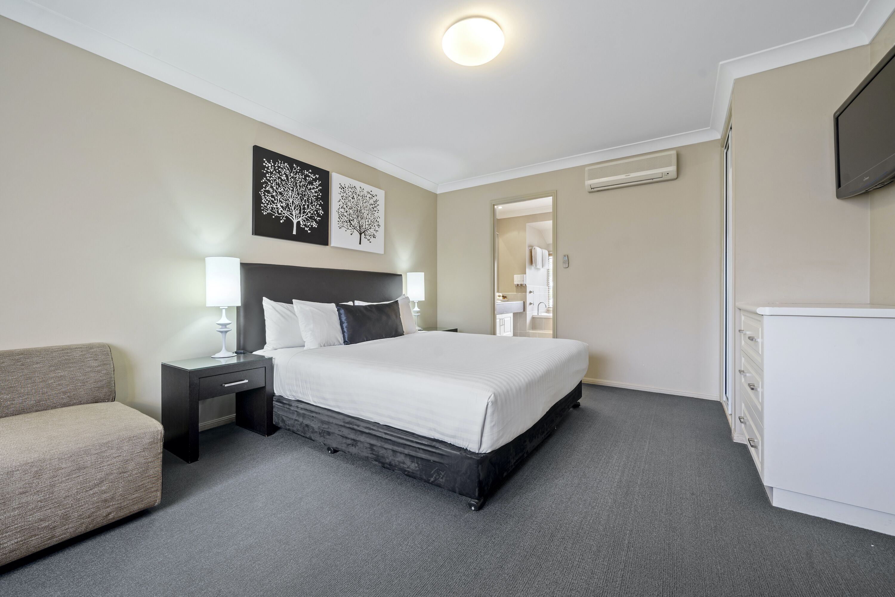 A hotel room with a bed, bedside table, lamp, and a dresser.