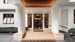 A modern building entrance with a wooden ceiling, large columns, and a stone pathway leading to the door. - House Sangkuriang (Bandung)