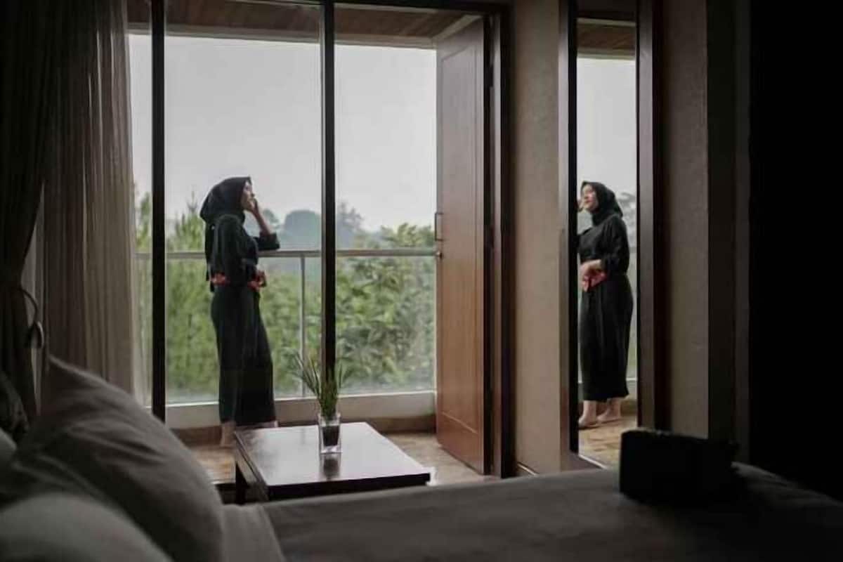 A room with a large sliding glass door, a bed, and a small table with a plant.