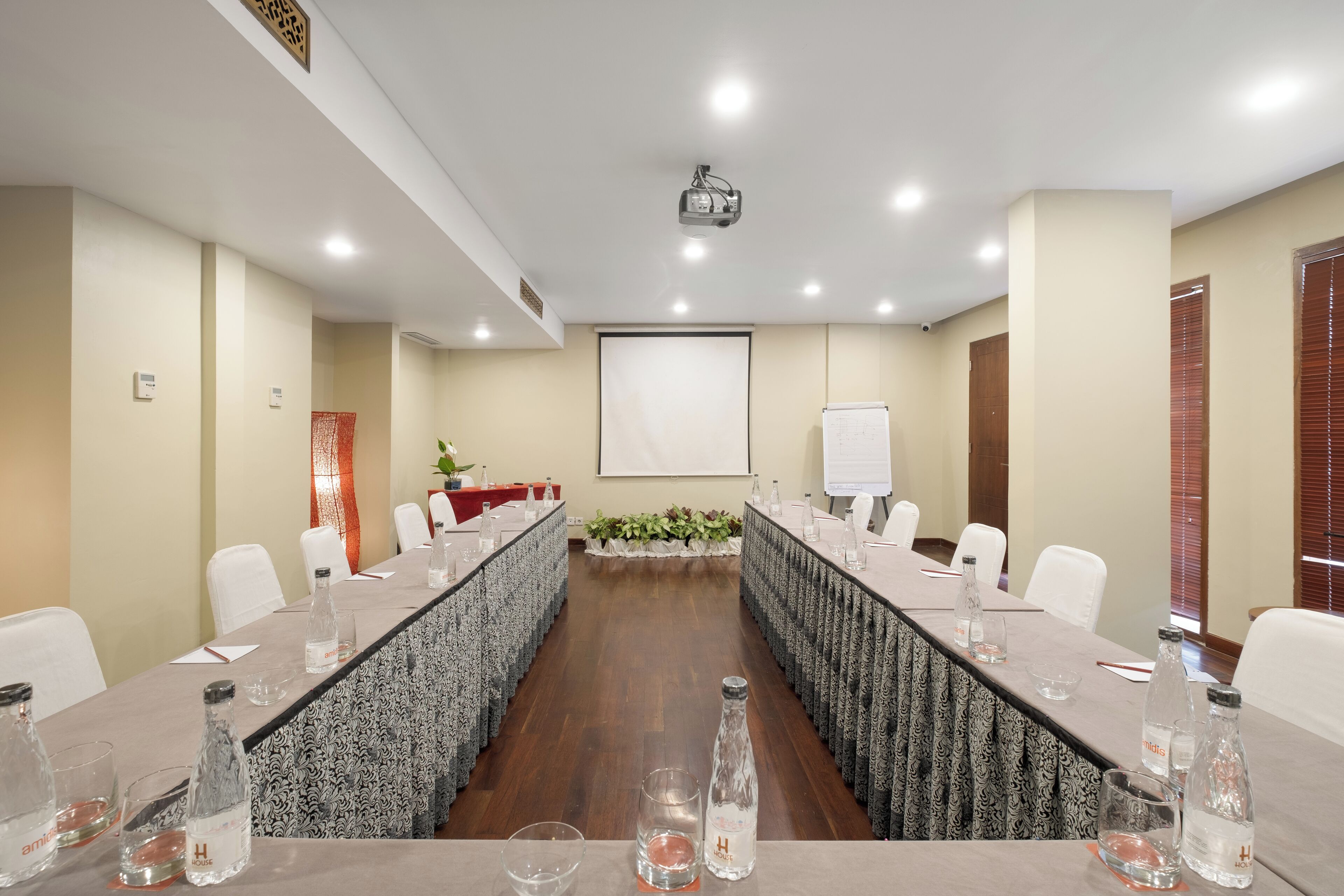 Una sala de conferencias con una larga mesa, sillas blancas y una pantalla de proyector.
