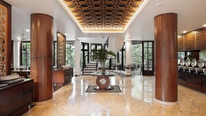 A spacious lobby with a marble floor, large wooden columns, a central decorative table, and a ceiling with a geometric pattern. - House Sangkuriang (Bandung)
