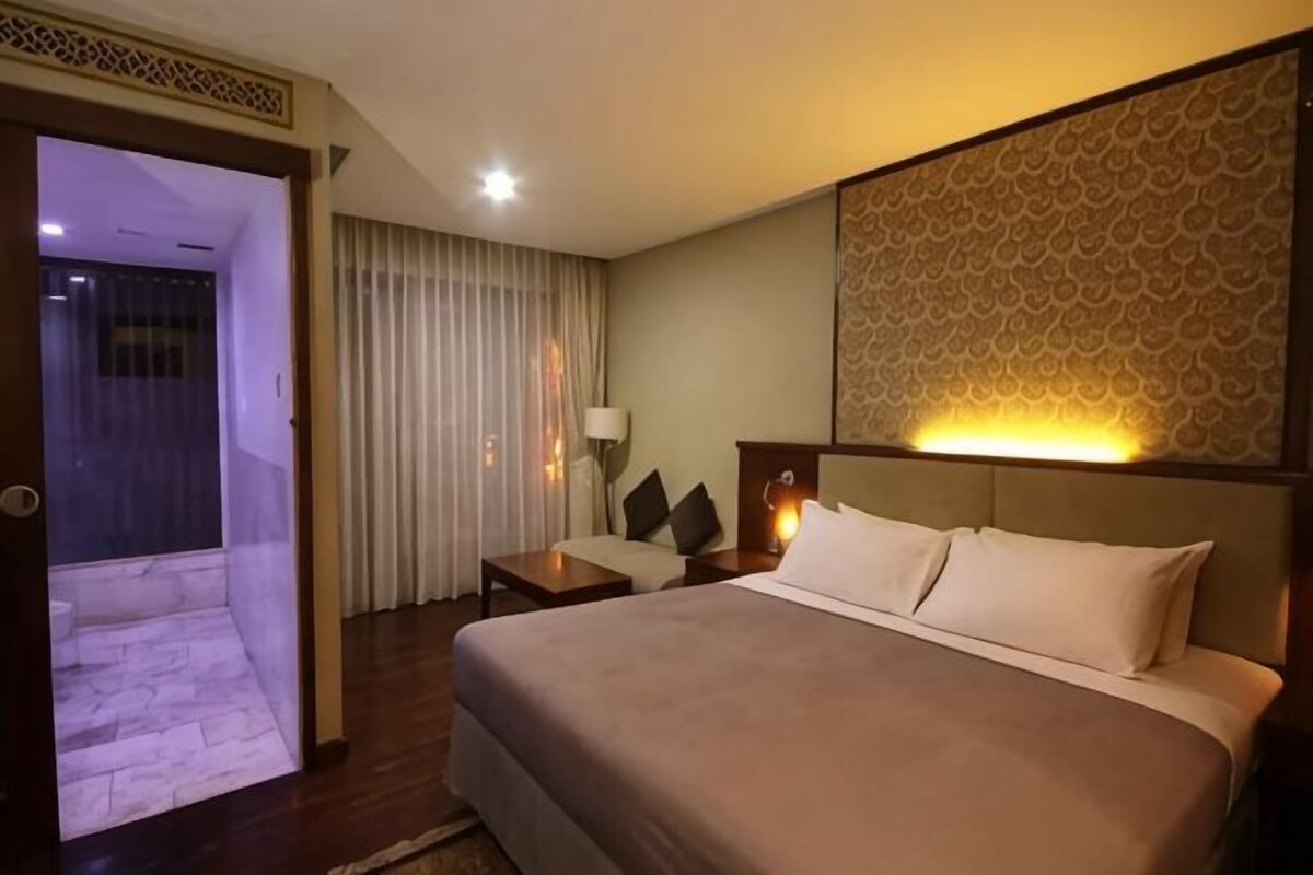A hotel room with a bed, a nightstand, a lamp, and a view of a balcony.