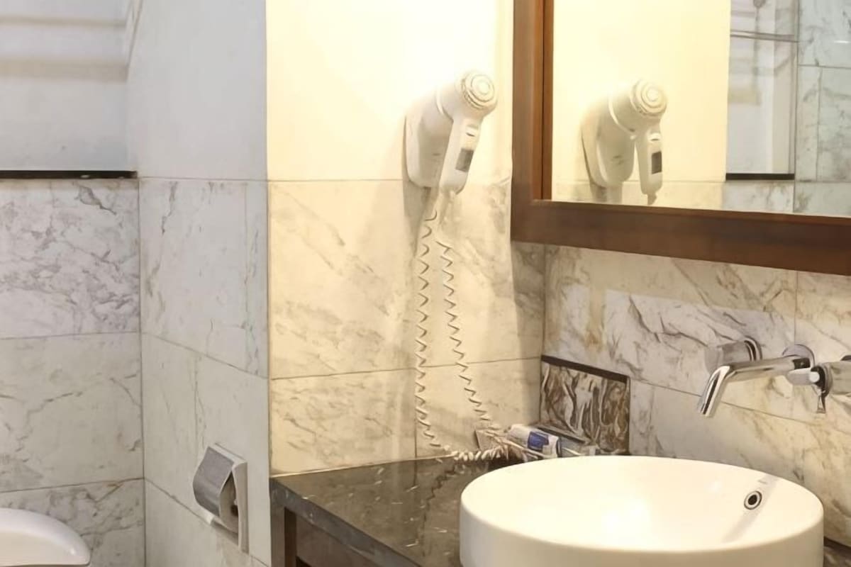 A bathroom with a marble wall, a sink, a mirror, a hairdryer, and a towel dispenser.