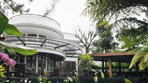 A modern building with a curved white exterior and a glass-enclosed terrace with outdoor seating. - House Sangkuriang (Bandung)