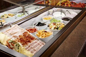 Buffet com diversas opções de comida, incluindo carnes, queijos, frutas e legumes.