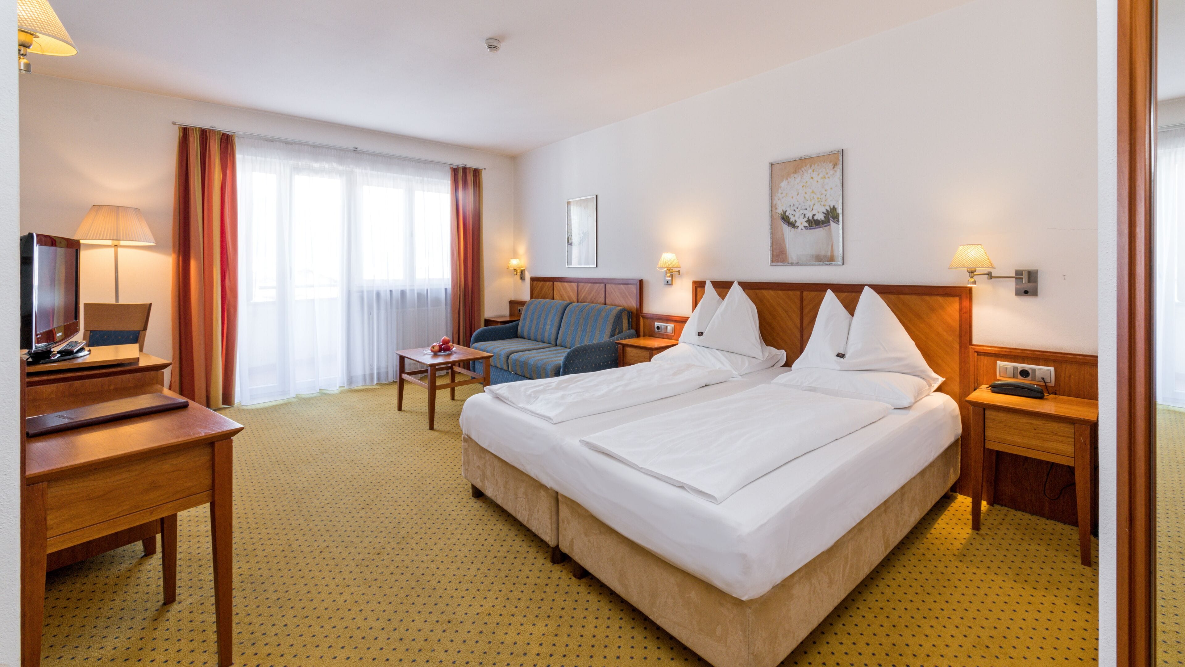 Habitació d'hotel amb un llit gran, un escriptori amb un ordinador, una cadira, una taula petita amb fruita i una televisió.